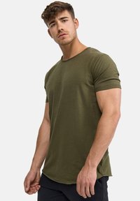 T-shirt verde oliva a maniche corte con scollatura rotonda, realizzato in tessuto morbido, caratterizzato da un orlo posteriore leggermente più lungo e una vestibilità rilassata.