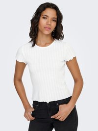 Bijeli pamučni top rebrastog uzorka s kratkim, valovitim rukavima i prianjajućim krojem. Uparen s crnim trapericama koje ističu glatku teksturu i čiste linije.