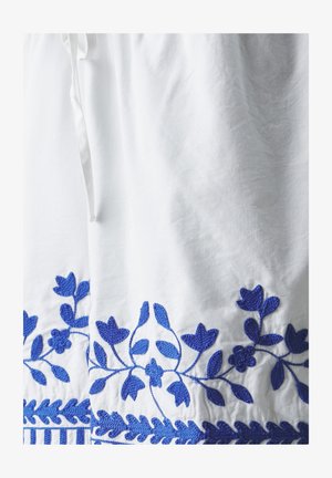 White fabric with detailed blue floral embroidery along the hem. Features a textured, woven pattern and a drawstring at the waist.