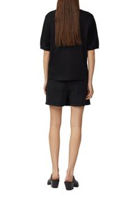 Czarny top z krótkim rękawem w połączeniu z czarnymi szortami o wysokim stanie. Ubranie ma luźny krój i miękką fakturę. Modelka nosi czarne mule.