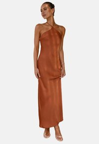  rostfarbendes Satin-Maxikleid mit Trägern, figurbetonender Silhouette und glatter Textur, der bis zu den Knöcheln reicht, getragen mit transparenten Sandalen.