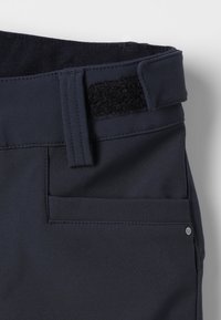 Mørkeblå bukser med en tekstureret talje, der har Velcro-lukning. En baglomme er synlig, sammen med en lille hardware-detalje.