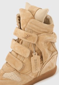 Sneaker compensée en daim couleur brun clair avec trois bandes Velcro, bout perforé, col rembourré et étiquette en daim "BRONX" suspendue à une chaîne à billes en métal.