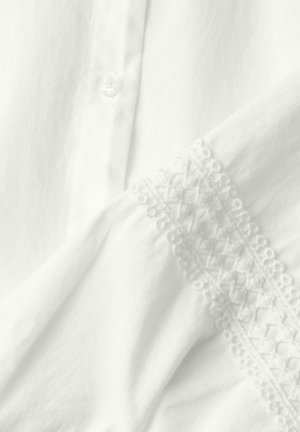 Tela blanca con un botón y ribete de encaje con patrones geométricos y florales a lo largo del borde.