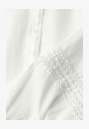 Tela blanca con un botón y ribete de encaje con patrones geométricos y florales a lo largo del borde.