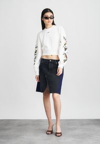 Biały krótkowłosy sweatshirt z kwiatowym haftem na rękawach, połączony z ciemnoniebieską spódnicą dżinsową z surowym wykończeniem. Czarte okulary przeciwsłoneczne dopełniają stylizację.