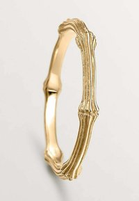 Anillo de oro con un diseño texturizado que recuerda al bambú. Presenta curvas suaves y acentos elevados, mostrando una forma única e intrincada.