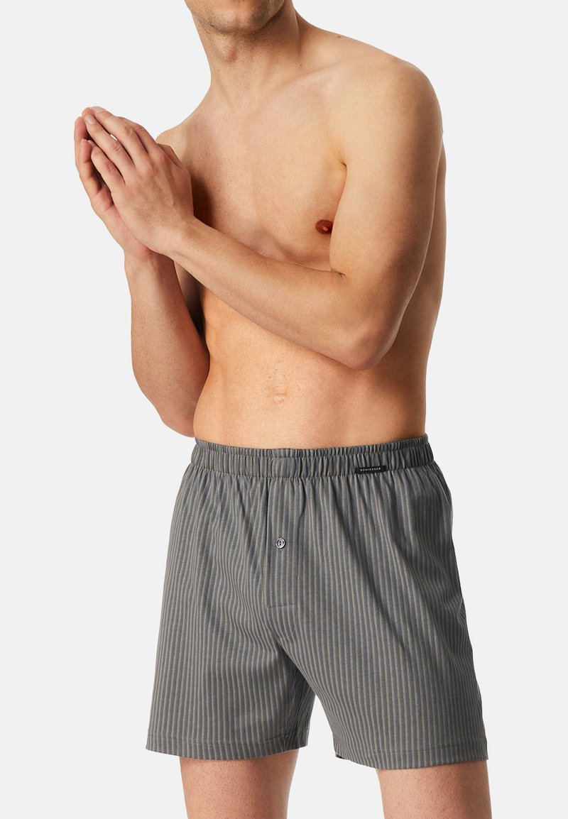 Boxer grigi a righe con elastico in vita e apertura con bottone. Il tessuto sembra leggero e ha una consistenza liscia.