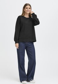 Felpa nera con maniche lunghe, scollo rotondo e spalle abbattute. Abbinata a jeans blu a gamba larga e sneakers bianche. Design semplice e casual.