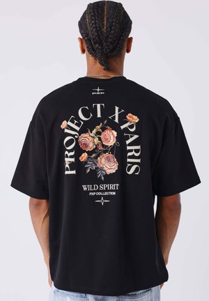 Camiseta de algodón negra con corte oversize. Presenta un gráfico floral colorido y el texto "PROJECT X PARIS WILD SPIRIT PXP COLLECTION" en la parte posterior.