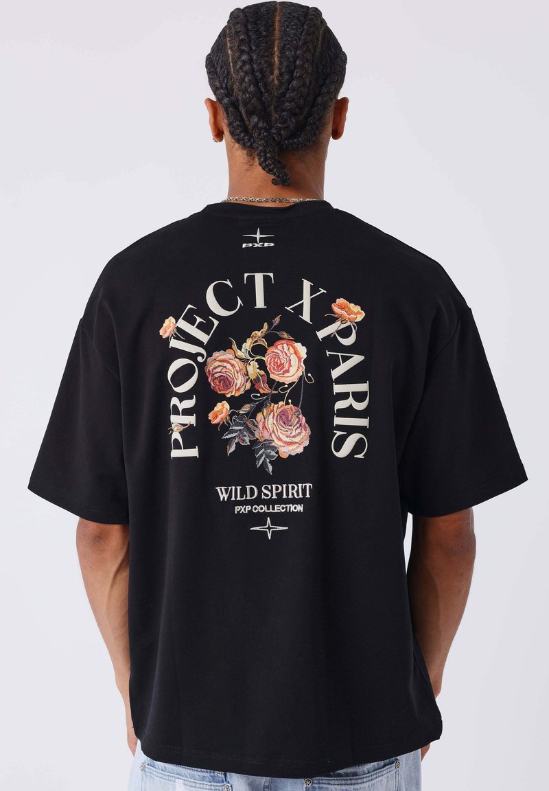 Camiseta de algodón negra con corte oversize. Presenta un gráfico floral colorido y el texto "PROJECT X PARIS WILD SPIRIT PXP COLLECTION" en la parte posterior.