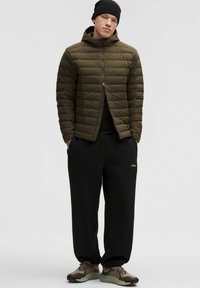 Giacca imbottita verde oliva con cappuccio, t-shirt nera, pantaloni della tuta neri e sneakers marroni con dettagli verdi. Texture liscia, design trapuntato.