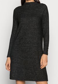 Vestito nero a maniche lunghe realizzato in tessuto testurizzato. Presenta un colletto alto e una vestibilità ampia, che arriva appena sopra le ginocchia. Dettagli minimi.