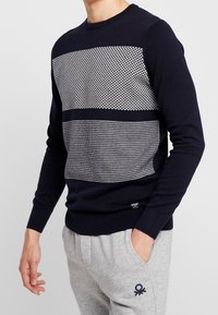 Marinblå tröja med strukturerade grå horisontella ränder och geometriska mönster. Ribbad mudd och fåll, figurnära design, tillverkad av stickad tyg.