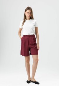 Witte T-shirt met ronde hals, gecombineerd met bordeauxrode shorts met hoge taille, plooien, zijzakken en een gladde textuur. Zwarte ballerina's maken de look af.