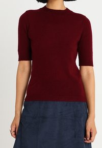 Burgundy lyhythihainen neulepusero, jossa on pyöreä kaula-aukko ja ribbausut sekä sininen teksturoitu hame.