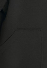 Zwarte hoodie met een kangoeroezak, een gladde textuur, een eenvoudig ontwerp en contrasterende stiksels langs de randen.