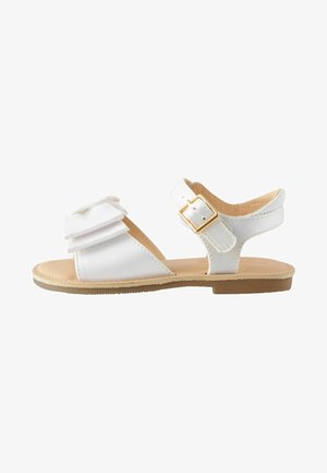 Sandal blanc avec un nœud en tissu superposé, une sangle à boucle et une semelle en caoutchouc plate. Présente une texture lisse et une semelle intérieure beige clair.