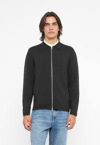 Casaco preto com fecho éclair, gola tipo colarinho e mangas longas. Feito de material suave, com uma textura lisa e um design minimalista.