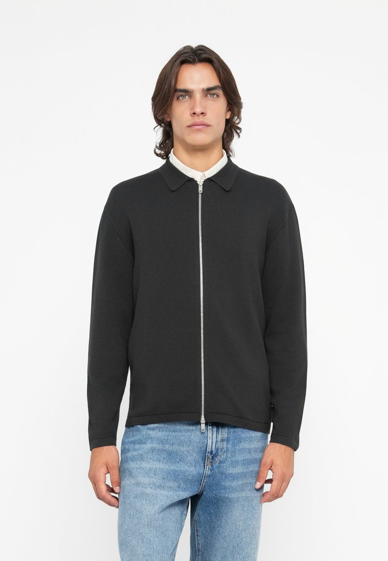 Casaco preto com fecho éclair, gola tipo colarinho e mangas longas. Feito de material suave, com uma textura lisa e um design minimalista.