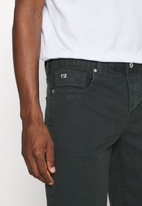 Butelkowozielone dżinsy z denimu o dopasowanym kroju, z niewielkim metalowym logo na przedniej kieszeni oraz standardowym układem pięciu kieszeni.