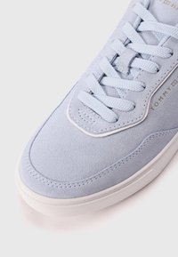 Hellblaue Wildledersneaker mit glatter Textur, flachen hellblauen Schnürsenkeln, runder Zehenpartie und weißer Gummisohle. Goldene Logo-Details sind enthalten.