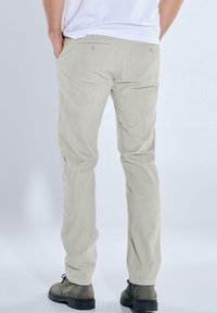 Helle beigefarbene Cordhosen mit geradem Bein, zwei Gesäßtaschen mit Knopfverschluss und einer weichen Textur. Tragen mit grauen Stiefeln.