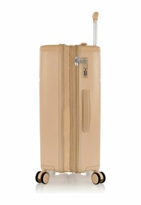 Valigia rigida beige con finitura testurizzata, manico retrattile e quattro ruote bianche e nere. Include una serratura a combinazione.