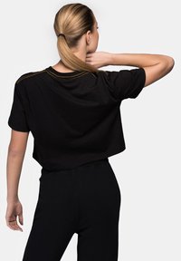 Black cropped t-shirt with short sleeves, featuring a round neckline and contrasting yellow stitching along the seams.
