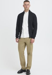 Cardigan cu fermoar, gri închis, textură moale; cămașă albă cu nasturi pe dedesubt; pantaloni bej; pantofi negri din piele. Design curat, modern.