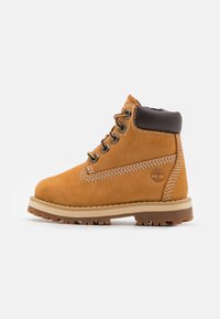 Beige Wildleder Stiefelknöchel mit einem braunen Lederkragen, runder Zehenform und kontrastierenden weißen Nähten. Verfügt über Metallösen und eine strukturierte Gummisohle.