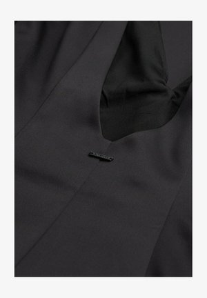 Black dress featuring a v-neckline, smooth fabric texture, and a small metal brand tag sewn into the front. Simple, streamlined design.