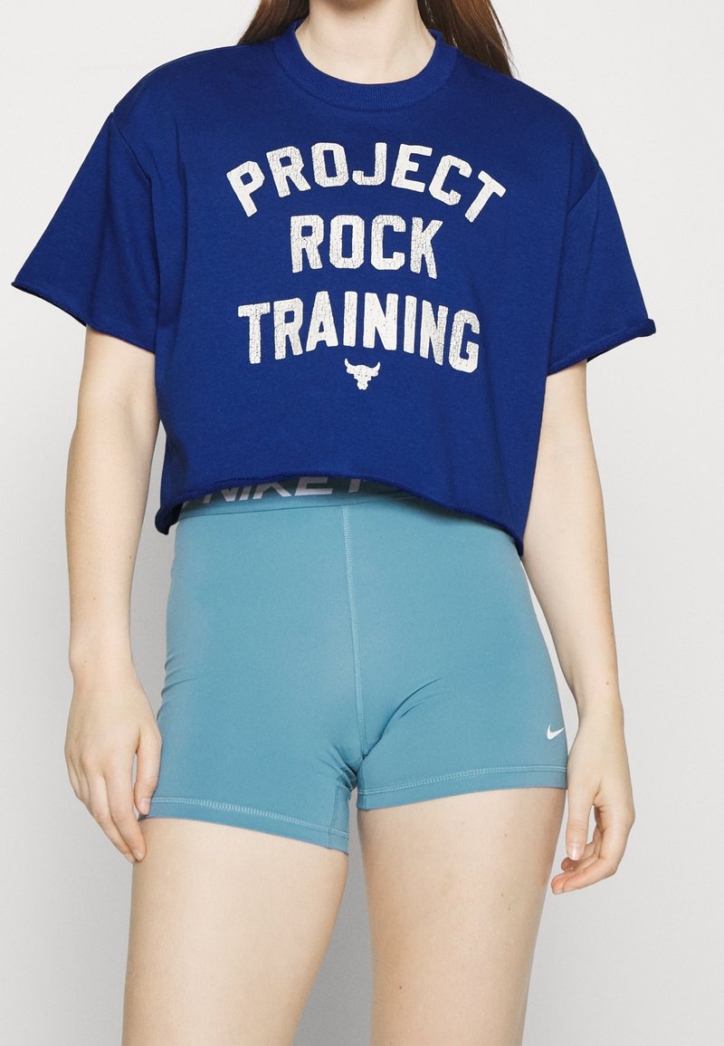 Blå kortärmad t-shirt med vit text "PROJECT ROCK TRAINING" och en tjur-logotyp. Kombinera med ljusblåa träningsshorts med en Nike-logotyp.