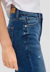 Jeansy z wysokim stanem w niebieskim odcieniu denim, lekko postrzępione, z kontrastującymi szwami, skórzaną łatą i pięcioma kieszeniami.