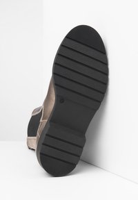 Semelle en caoutchouc noir avec grip texturé, tige en daim marron clair contrastant, forme arrondie, avec des accents cousus le long des coutures. Taille marquée 37.