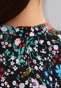 Svart blommig klänning med en färgglad botanisk tryck av rosa, röda och blå blommor, samt en dragkedja i ryggen vid halslinningen.