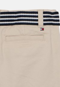 Pantalon kaki avec une ceinture rayée bleu marine et blanche, doté d'une poche arrière et d'une petite étiquette logo. Le tissu présente une finition texturée.