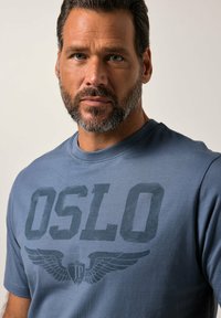 Modré bavlněné tričko s velkým grafickým potiskem slova "OSLO" s designem křídel pod ním. Krátké rukávy a kulatý výstřih.