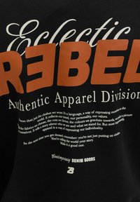 Must kangas julgete sõnadega "Eclectic REBEL" oranžis ja valges, millele järgneb tekst riietusest, mis väljendab isikupära ja individuaalsust.