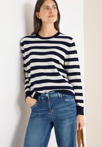 Marineblauer und weiß gestreifter Pullover aus weichem Stoff mit Rundhalsausschnitt und gerippten Bündchen, kombiniert mit hellblauen Jeans aus Denim.