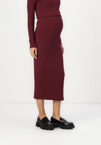 Burgundská pletená těhotenská blůza s rib strukturou a midi sukně s přiléhavým střihem. Černé masivní mokasíny dotvářejí outfit.