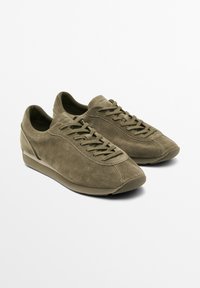 Olivgrüne Wildledersneaker mit runder Zehenpartie, flachen Schnürsenkeln und minimalistischem Design. Verfügt über ein strukturiertes Obermaterial und eine gepolsterte Sohle.