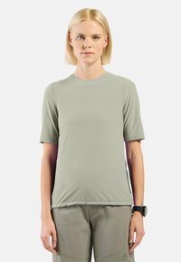 Lichtgroene T-shirt met korte mouwen, een vlakke brei textuur en een ronde halslijn, gecombineerd met lichtgrijze broek, weergegeven tegen een witte achtergrond.