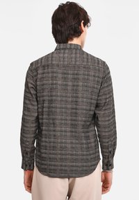Camicia a quadretti in tonalità di grigio scuro e marrone, con colletto a punta, maniche lunghe e polsini con bottoni. La texture è in tessuto intrecciato.