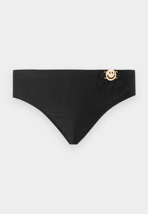 Mustad bikiinipõhjad, kellel on väike kuldne naeratava näo ripats, mis on kinnitatud vöökoha lähedale paremal pool.