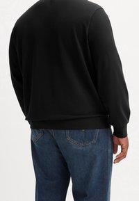 Felpa nera con polsini e orlo a coste, abbinata a jeans in denim blu con taglio classico e due tasche posteriori.