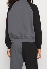 Grå och svart färgblockerad sweatshirt med hög krage, ribbade ärmslut och midja; mjukt sweatshirtmaterial med en avslappnad passform.
