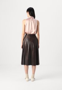 Blusa senza maniche in satin rosa abbinata a una gonna plissettata in pelle marrone scuro, che mette in evidenza una texture liscia e variazioni di colore uniche.