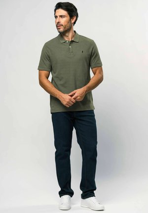 Olívazöld galléros póló kétgombos sliccel, rövid ujjal és kis emblémával. Sötétkék farmerral és fehér tornacipővel párosítva.