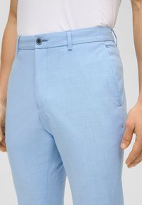 Hellblaue Hose aus glattem Stoff, mit flachem Bund, einem Knopfverschluss und seitlichen Taschen.